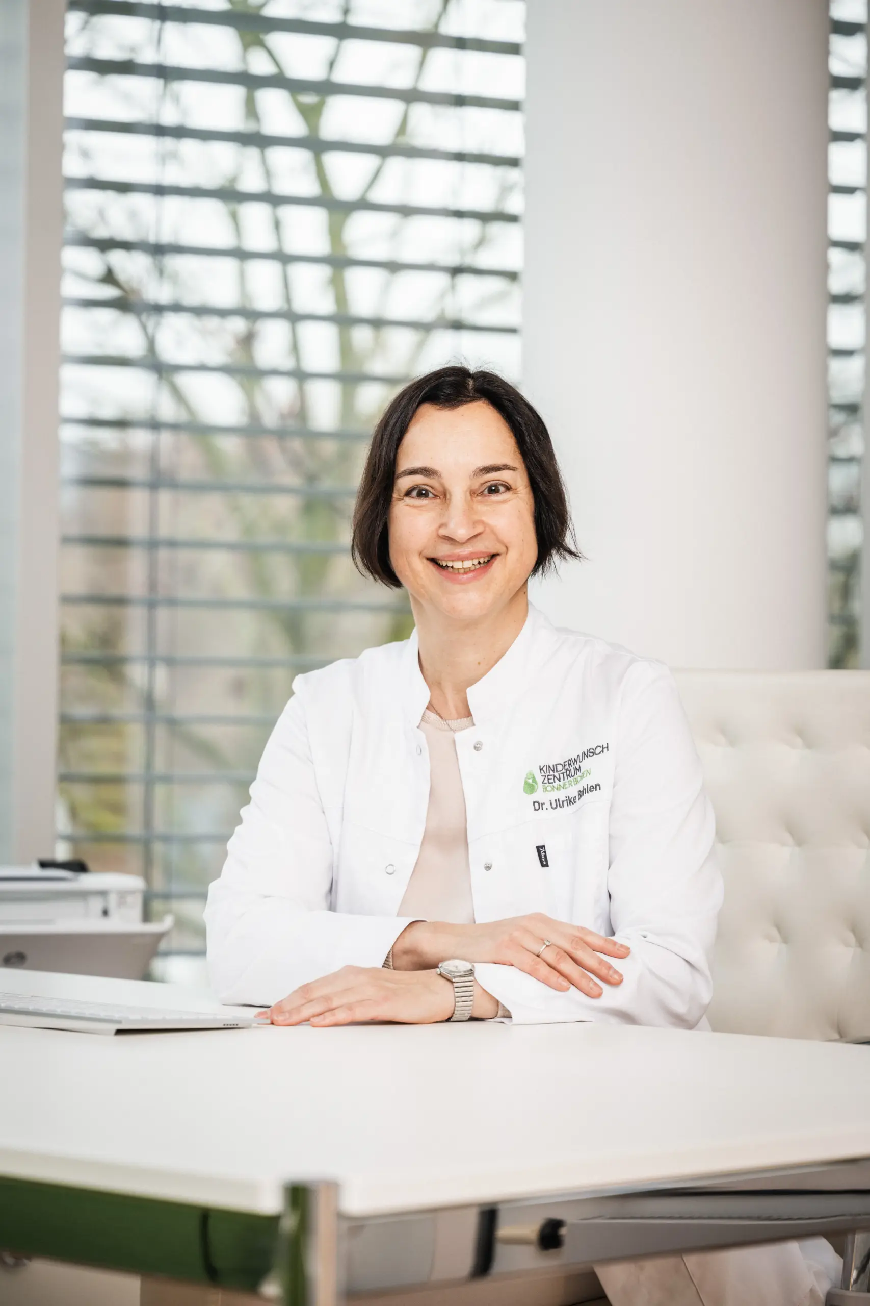 Frau Dr. Bohlen mit einem Lächeln am Schreibtisch und überkreuzten Armen im Kinderwunschzentrum Bonn horizontal